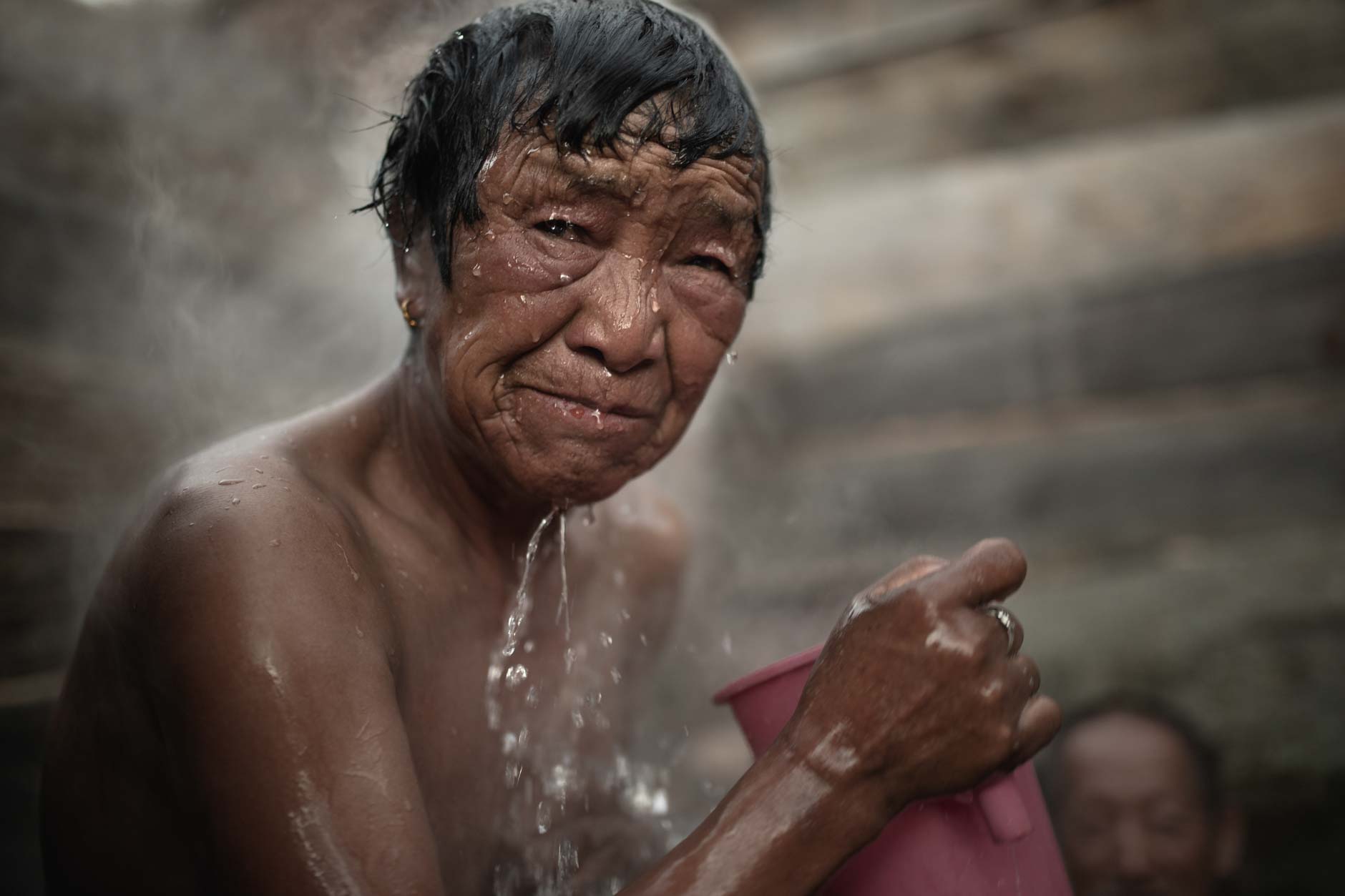 Portrait photography of an elderly Bhutanese woman taking a traditional hot stone bath in a village in Bhutan