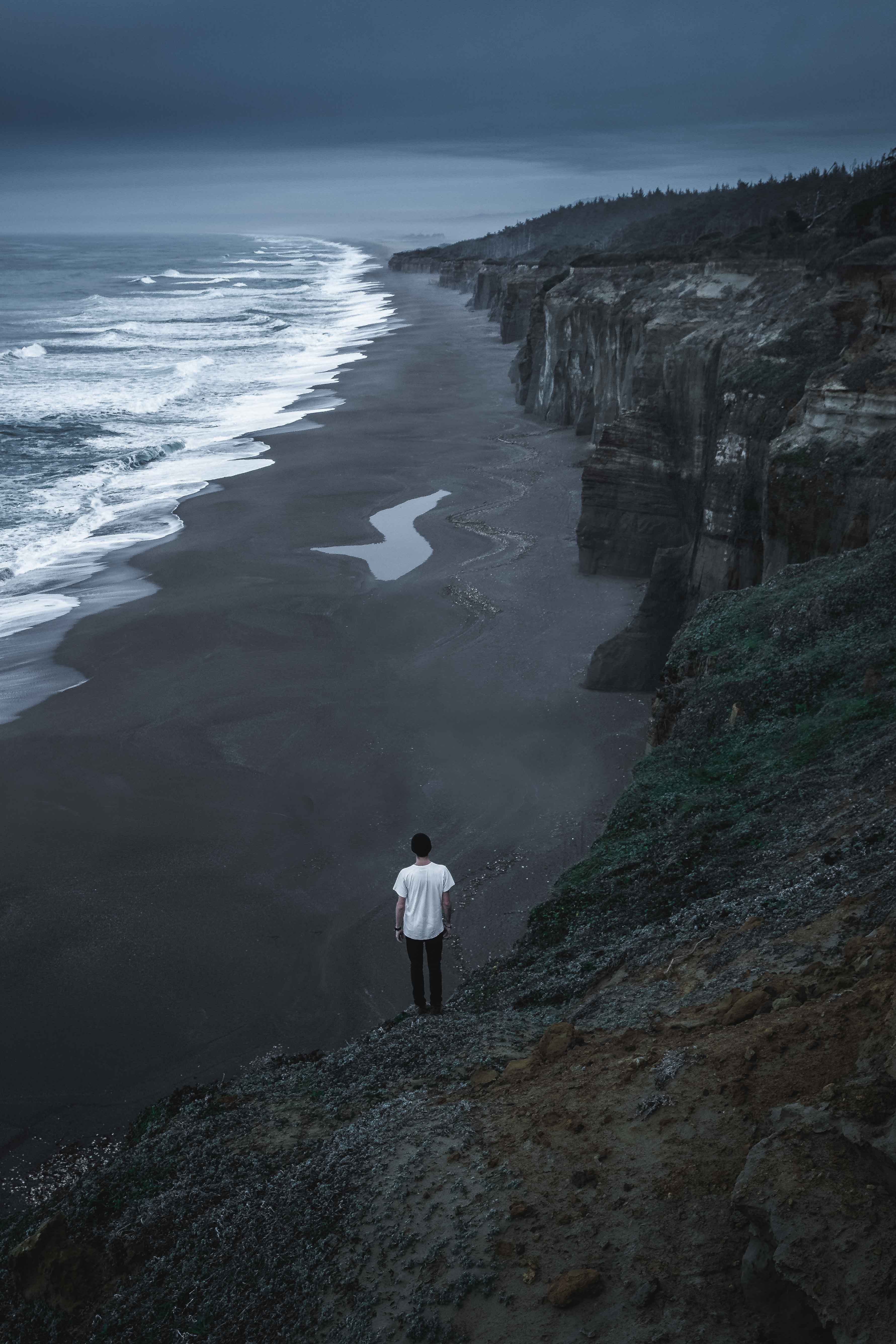 A person wearing a white tshirt looks out at the Southern Oregon coastline