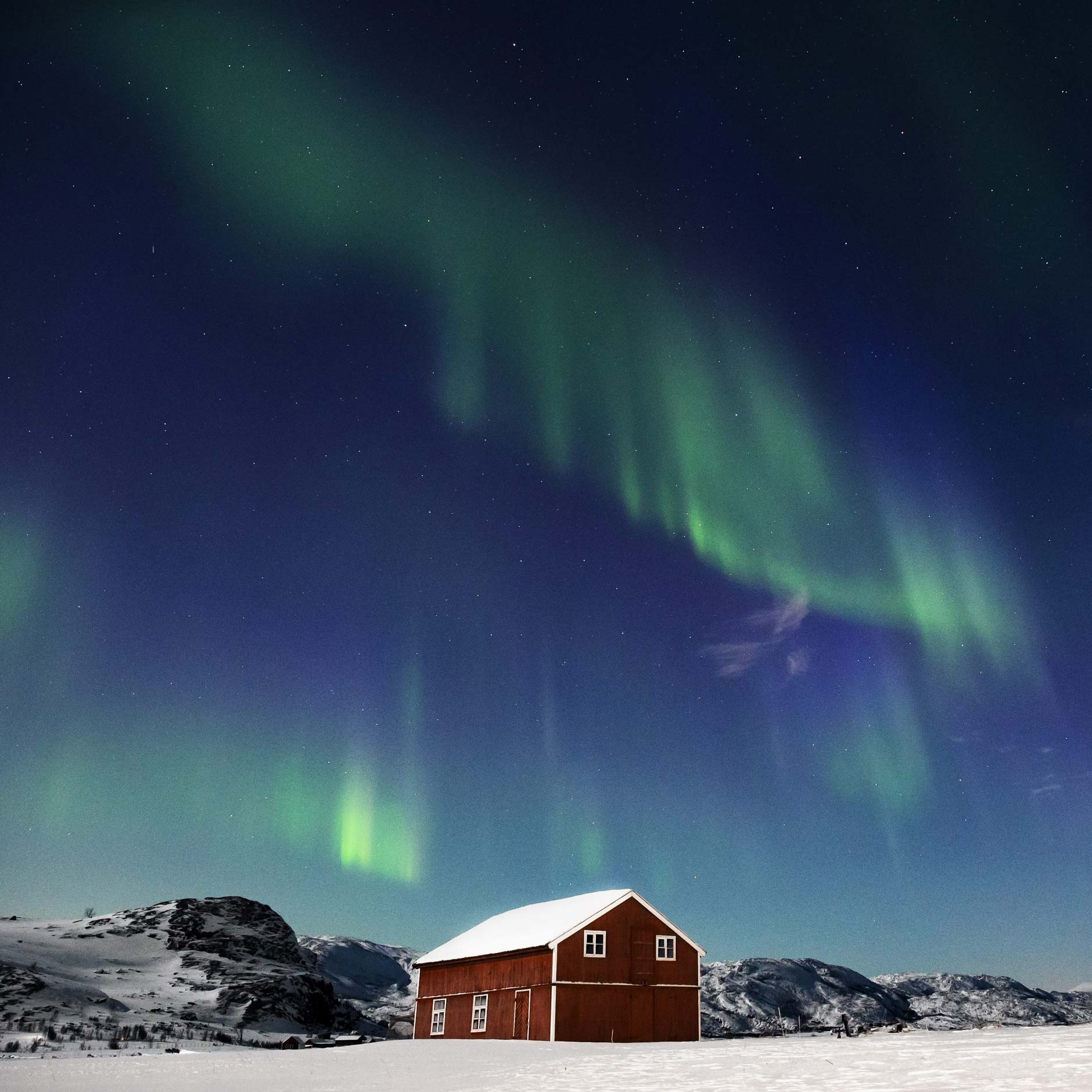 The aurora borealis over a red cabin in the snow in Norway at night