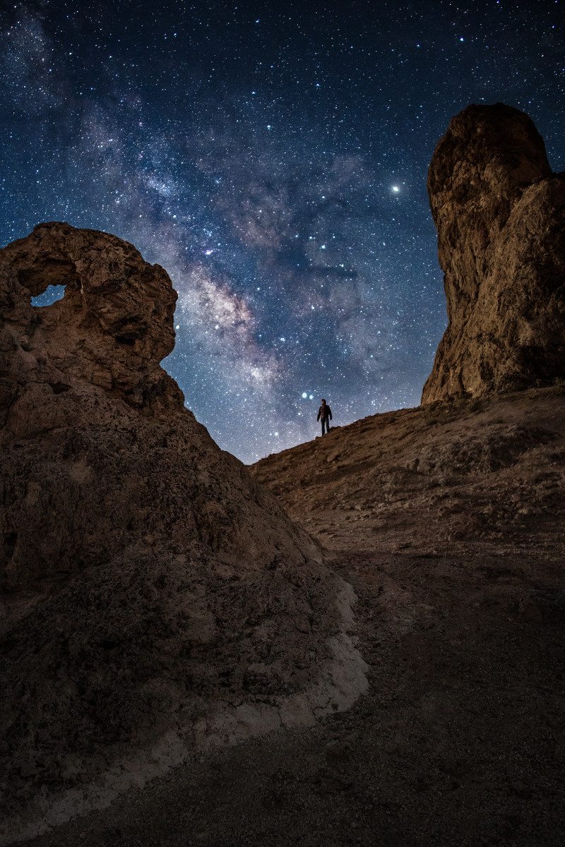 Night photography of a person standing below the milkyway at the Trona Pinnacles in California