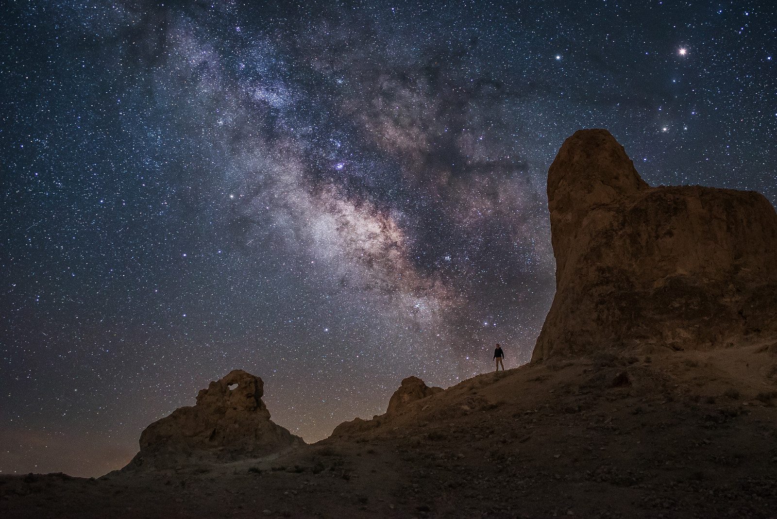 Night photography of a person standing below the milkyway galaxy and stars in the trona pinnacles, California Photo by Andrew Studer