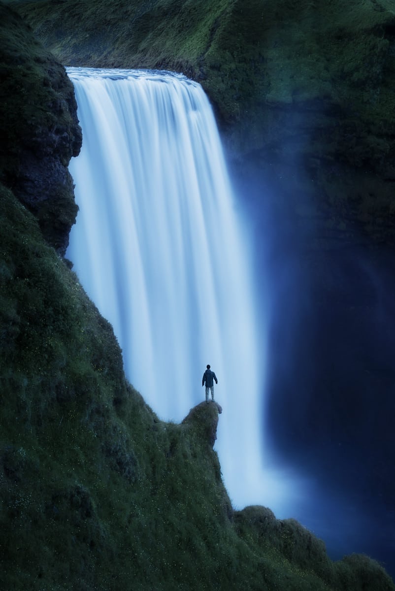 Photography of a A person stands next to Skogafoss waterfall in Iceland