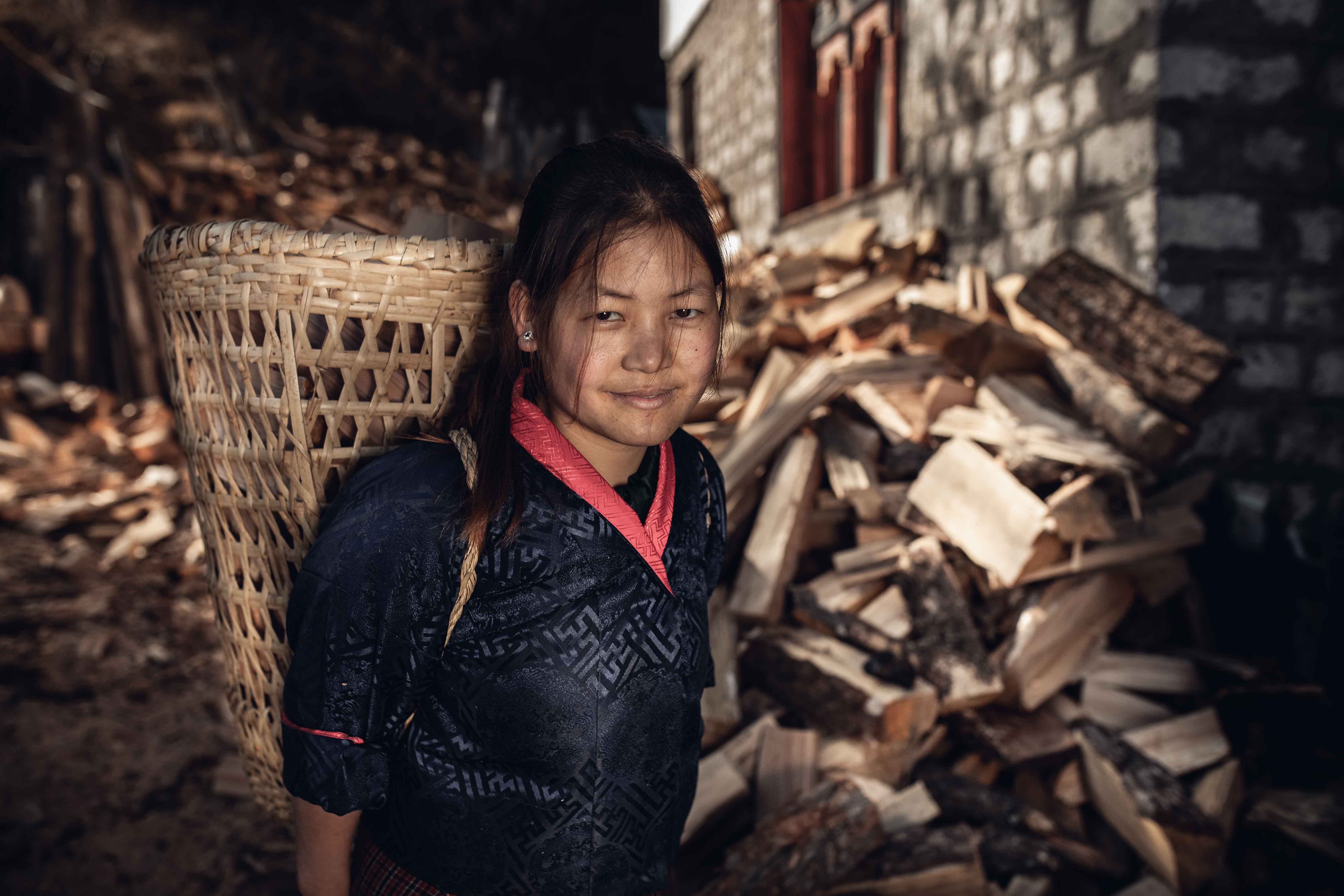 Portrait photography of a young Bhutanese girl carrying firewood on her back