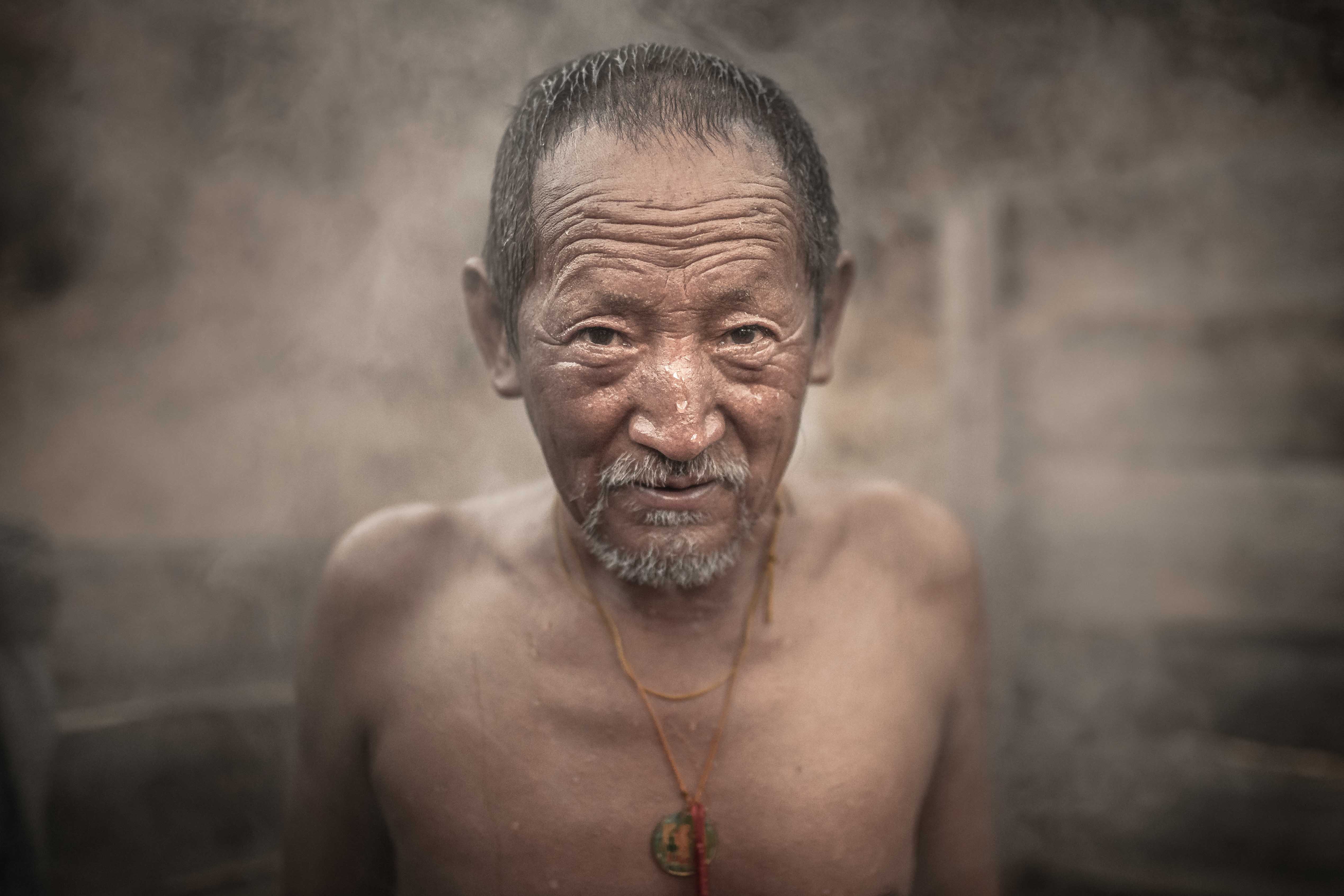 Portrait photography of a Bhutanese man taking a hot stone bath in a village
