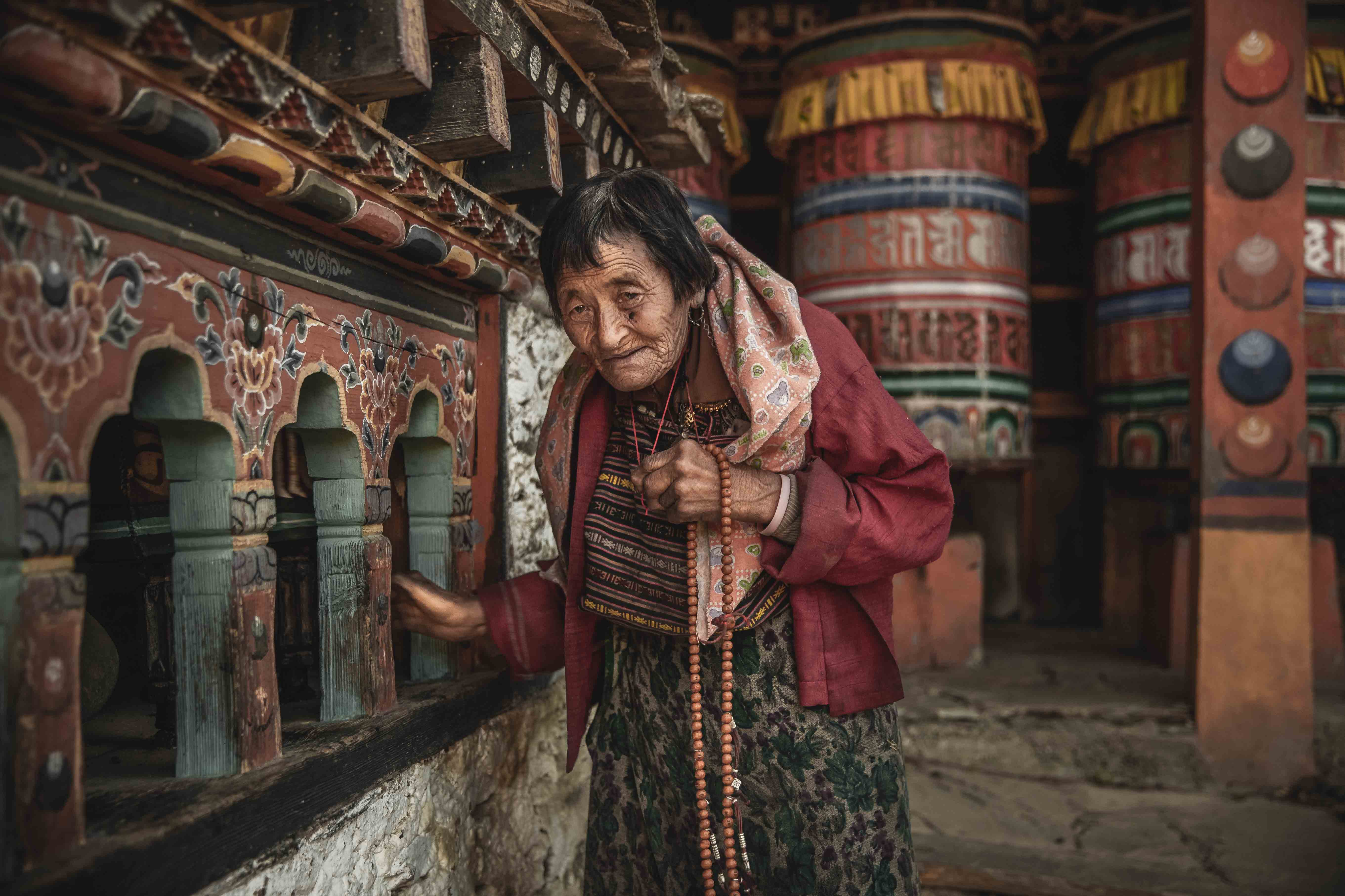 Portrait photography of an elderly Bhutanese woman at a temple near Bumthang, Bhutan. She is spinning a prayer wheel