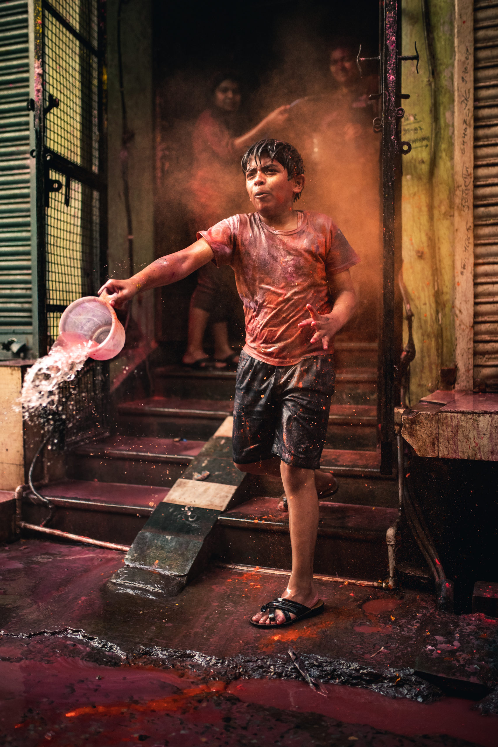 Street photography of a young boy throwing a bucket of water in the streets during the Holi Festival in Vrindavan, India