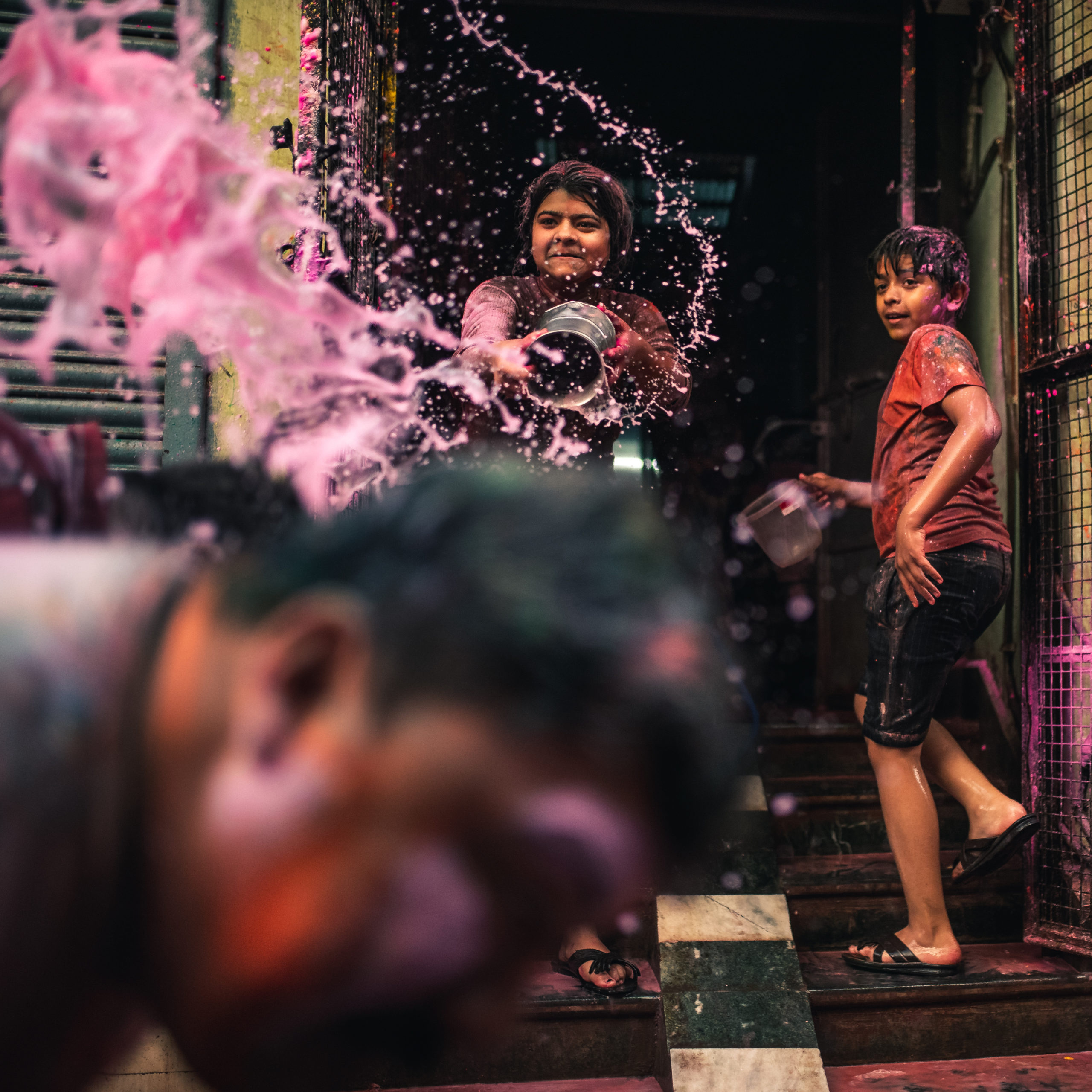 Street photography of a girl throwing a bucket of colorful water at a man in the streets of Vrindavan, India during the Holi Festival