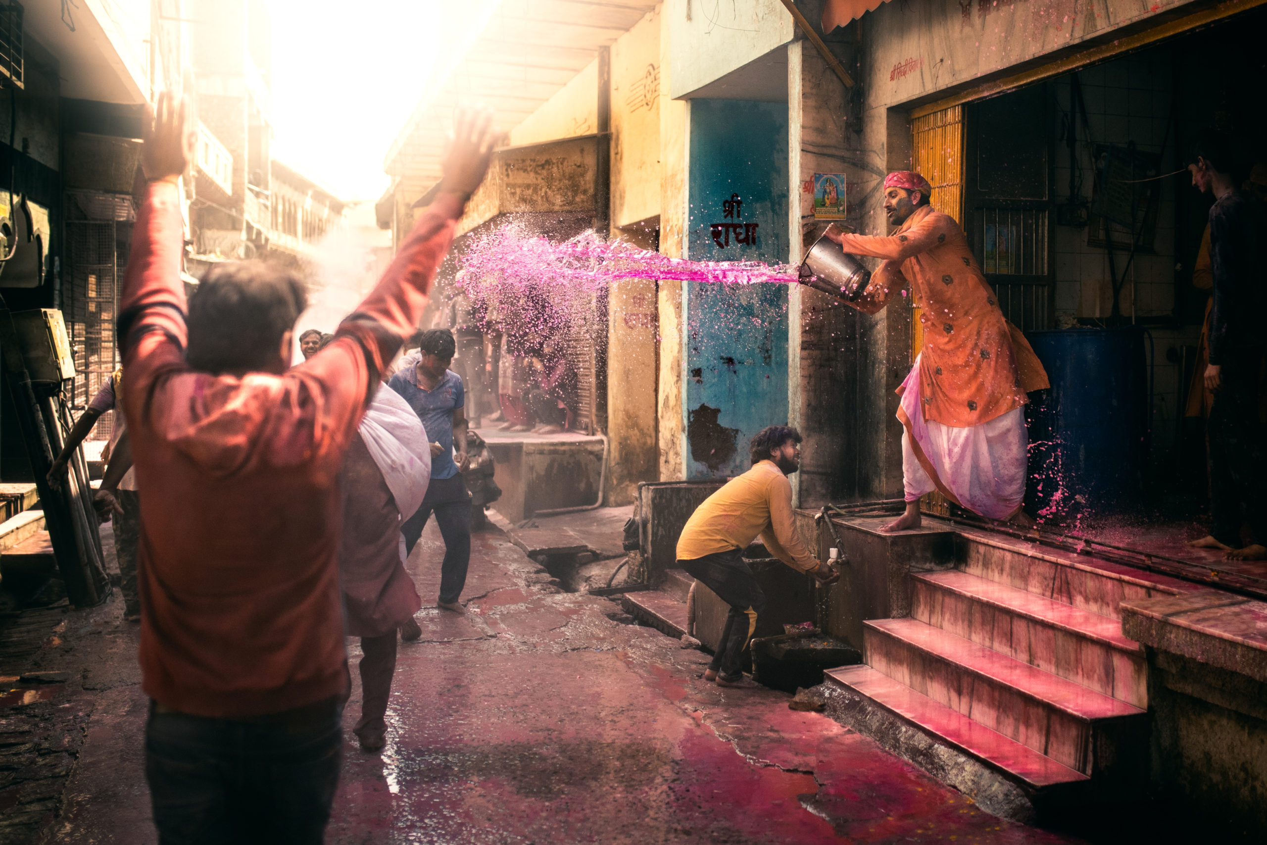 Street photography of a man throwing a bucket of water at someone in the streets during the Holi Festival in Vrindavan, India