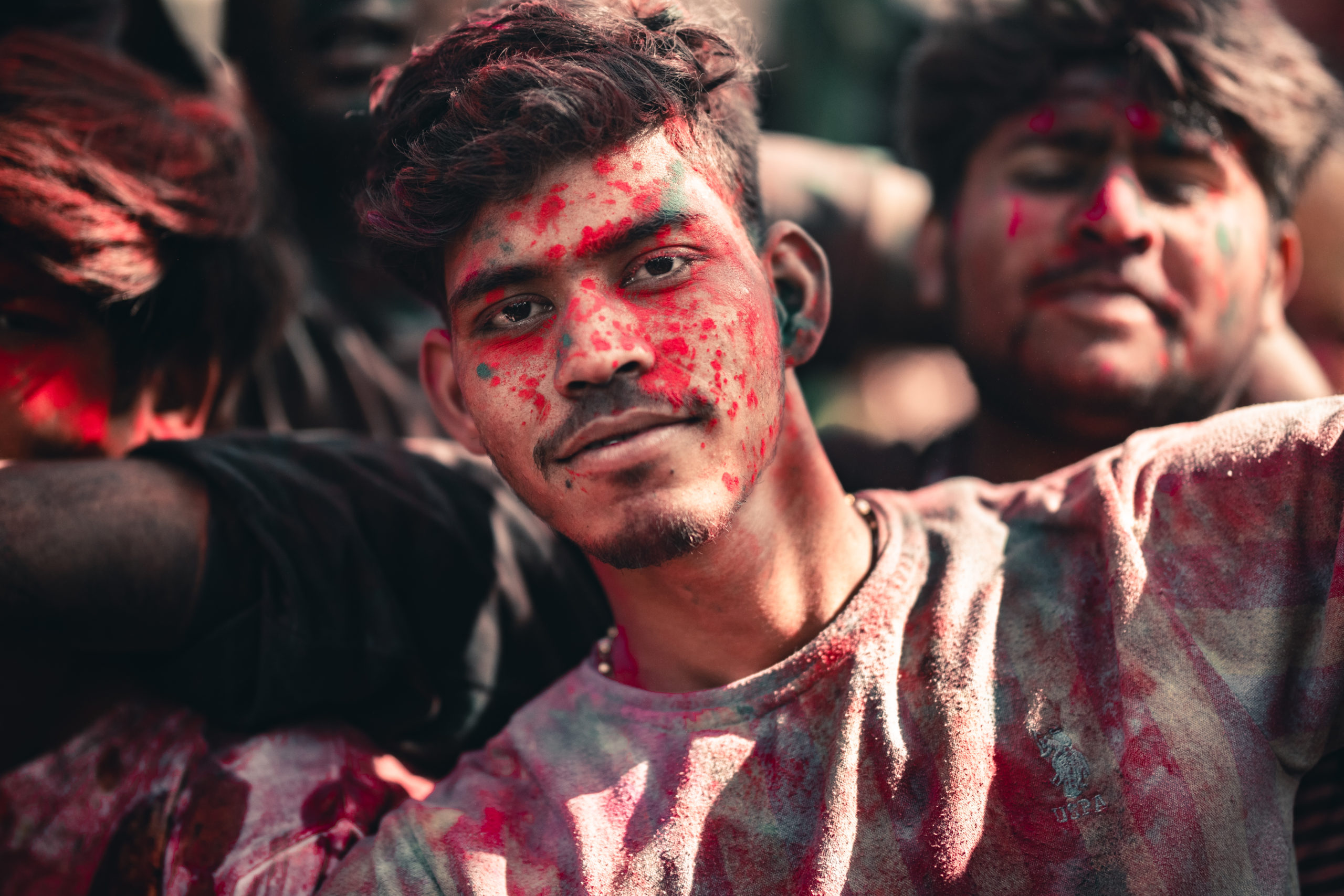 Street photography of a man celebrating the Holi Festival in a temple in Gokul, India. The man has colorful holi powder all over his face and shirt
