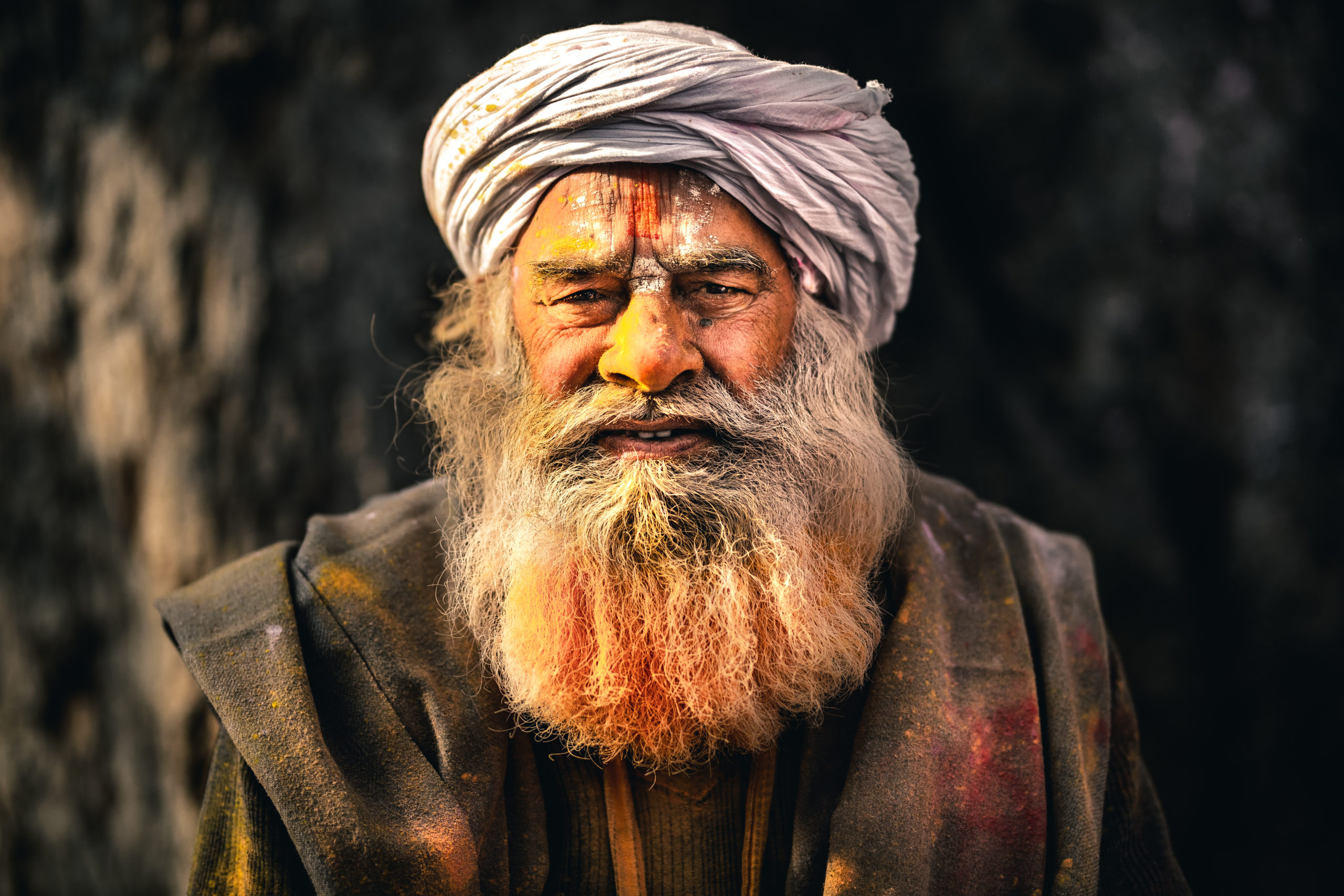 Street Portrait Photography of an elderly man in Mathura, India during the Holi Festival. He has color on his face and in his beard