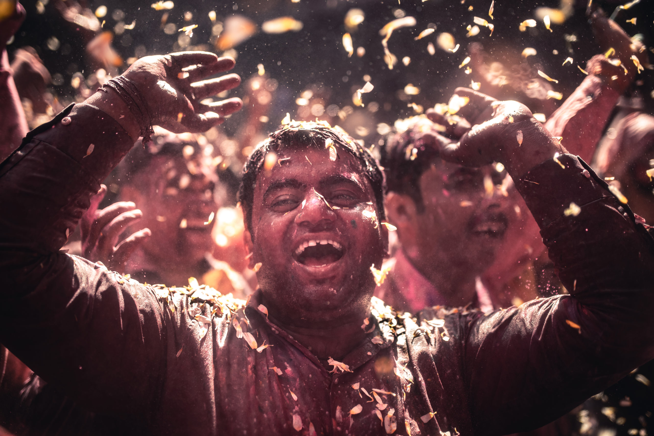 Street photography of a joyful man celebrating the Holi Festival in Vrindivan, India as flower pedals fall from above