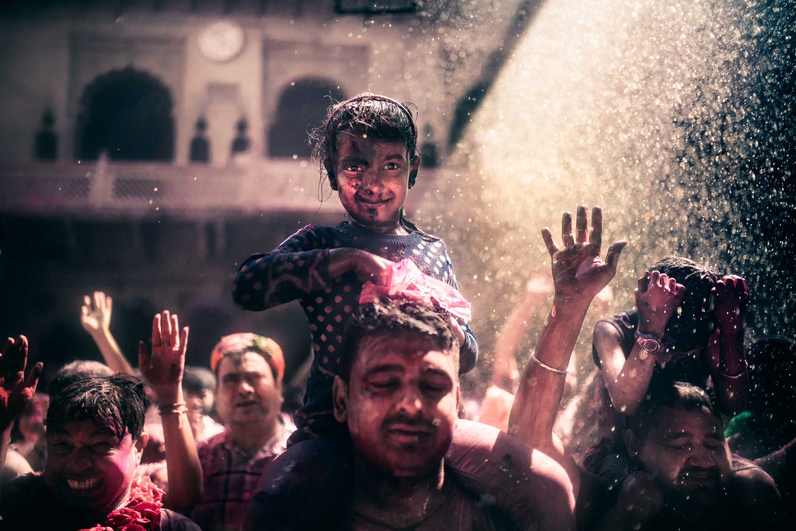 Street Photography of a young girl on her father's shoulders celebrating the Holi Festival of colors in Vrindivan, India