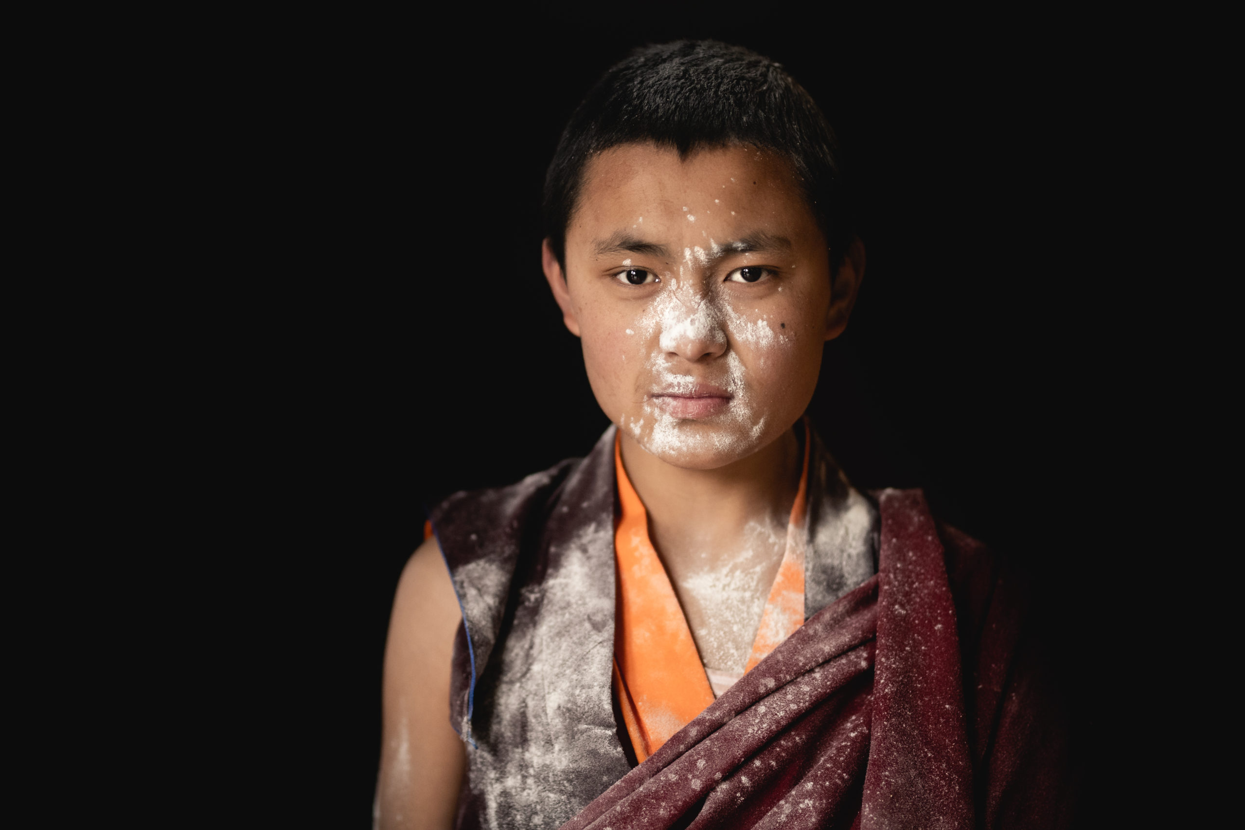 Portrait photography of a young monk in Bhutan with flour on his face and robes from the Losar Festival