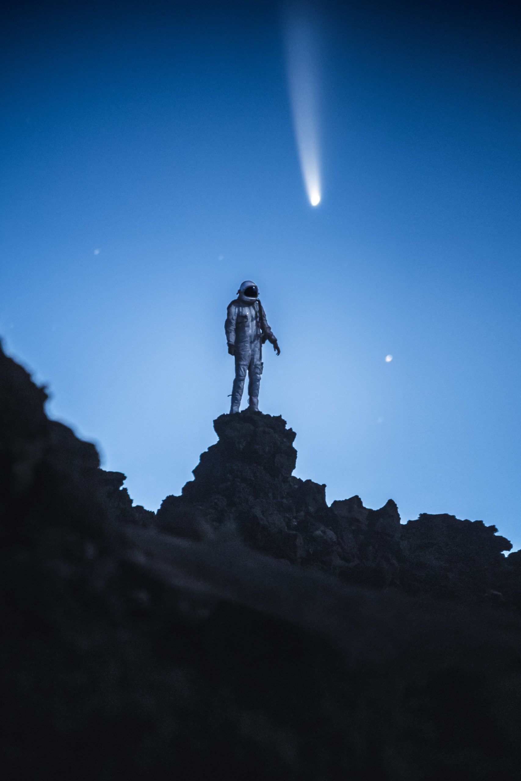 Photography of an astronaut stands on a rock as Comet Neowise 2020 passes above. Image by Andrew Studer