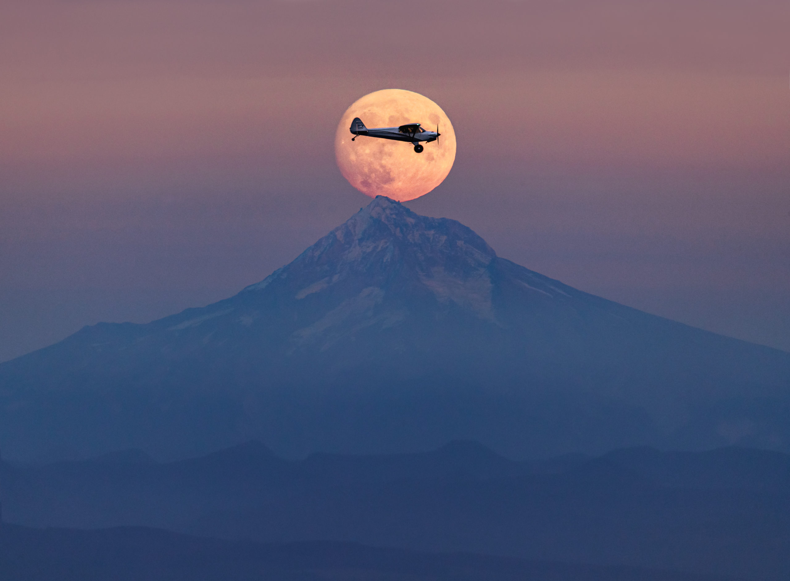 Aviation photography of a Carbon Cub airplane inside the rising full moon at sunset over Mount Hood, Oregon