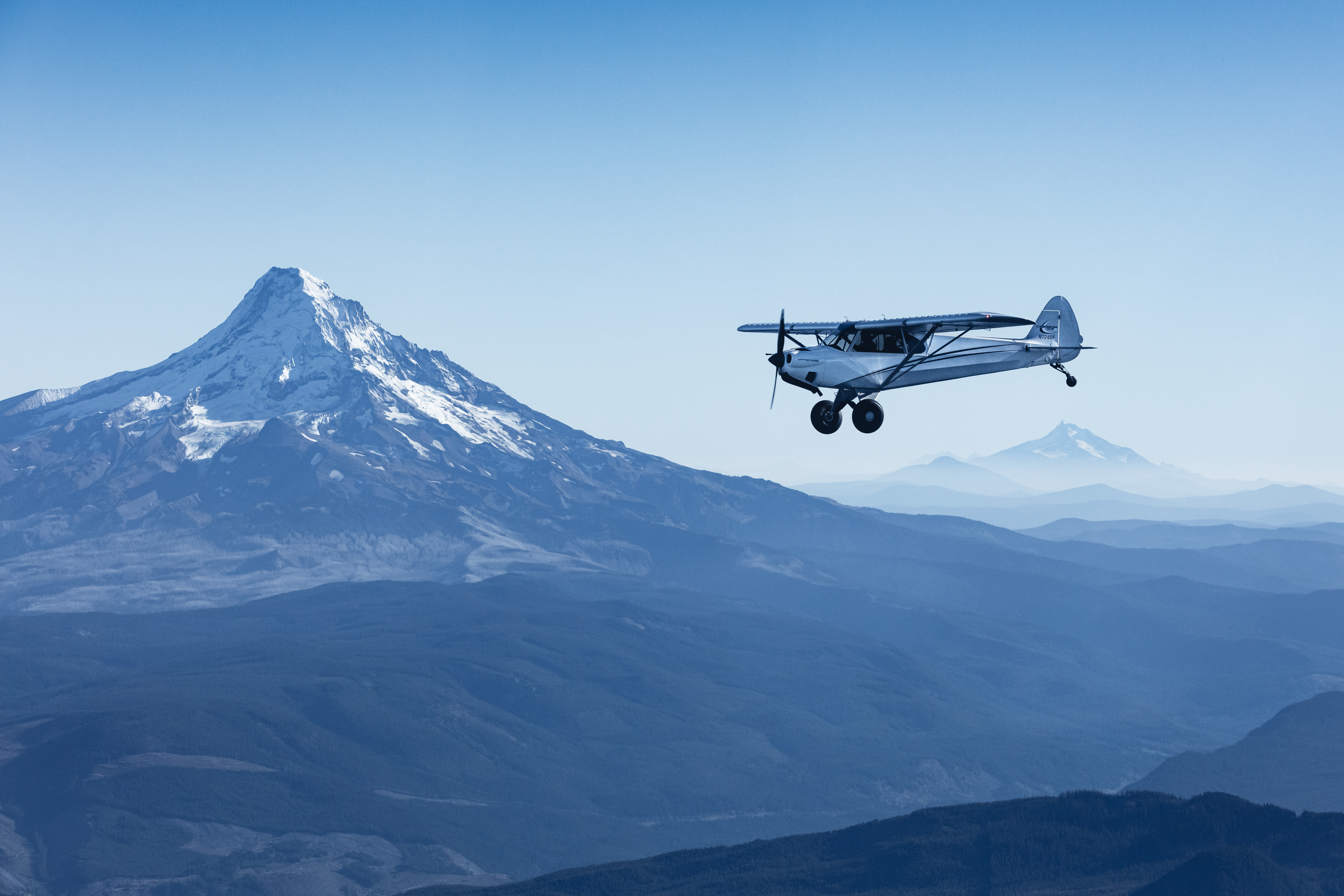 Aviation photography of a carbon cub airplane flying over Mount Hood and Mount Jefferson, Oregon
