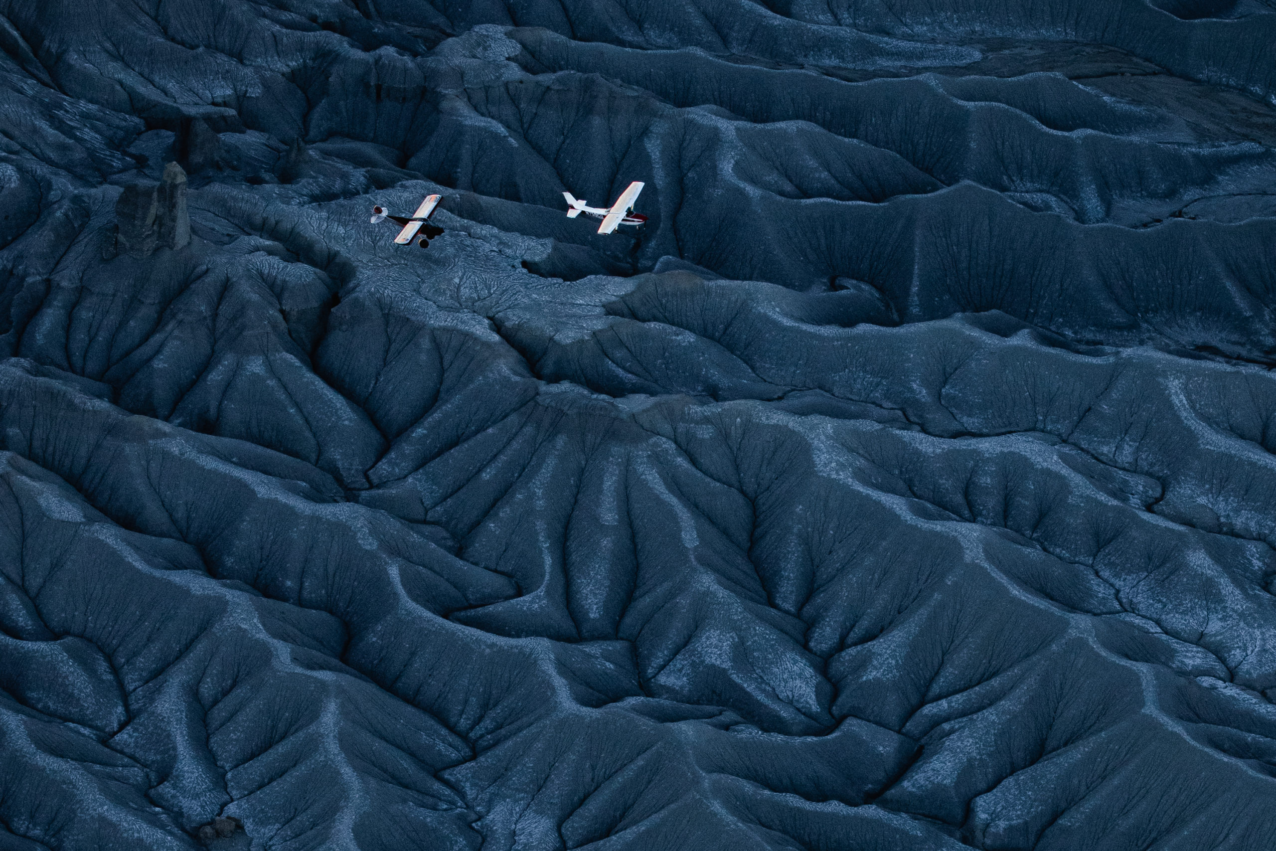 Photography of two airplanes flying low over the beautiful valleys and ridge-lines of Factory Butte, Utah