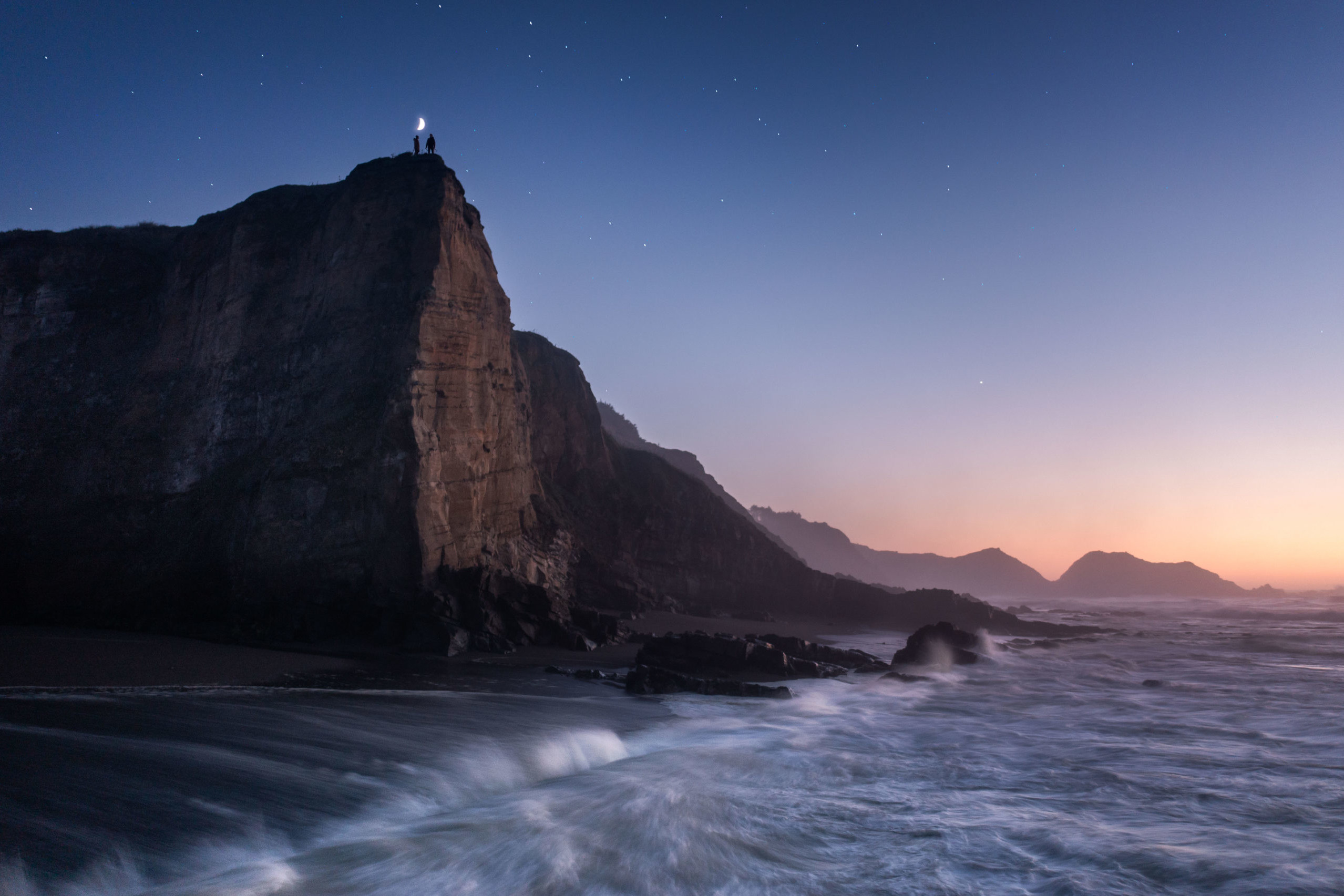 Landscape photography at night of two people standing on a beautiful cliff on the Oregon Coast during a starry night.
