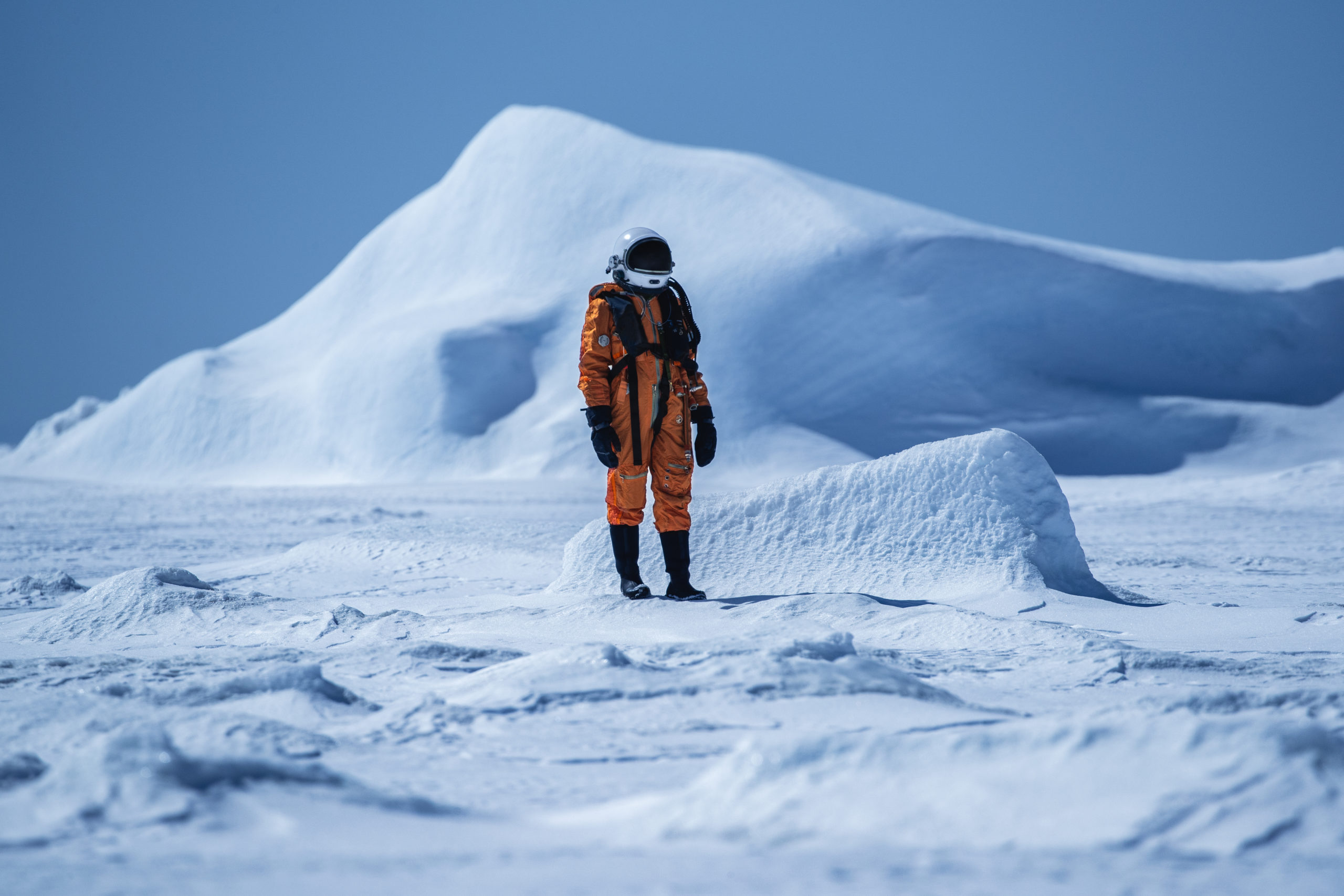 Conceptual photography of an astronaut in an orange spacesuit from Space to Roam standing in a frozen landscape in Antarctica