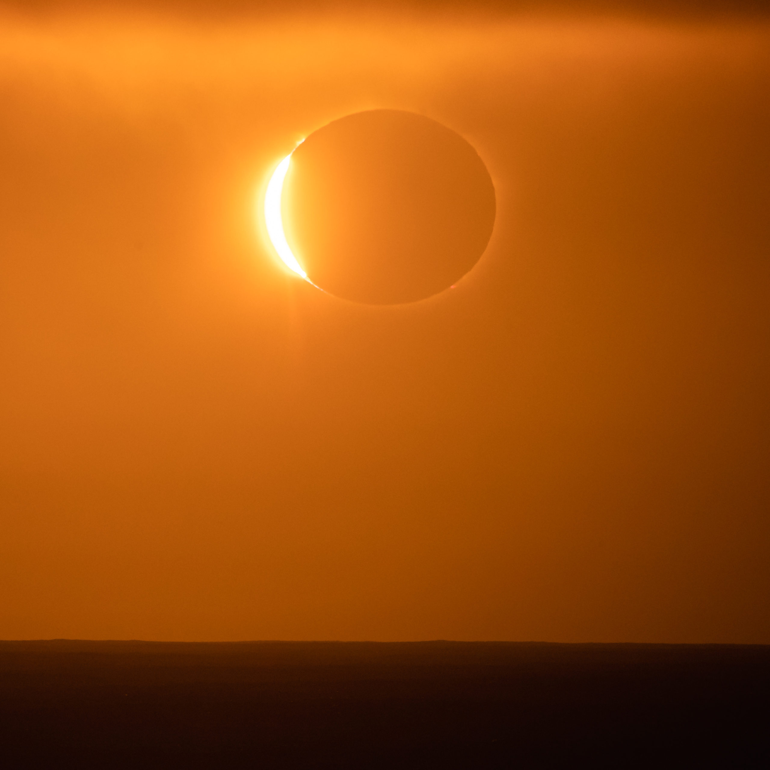Photography of the total solar eclipse occurring just above the horizon over the ocean during sunrise in Antarctica on December 4 2021