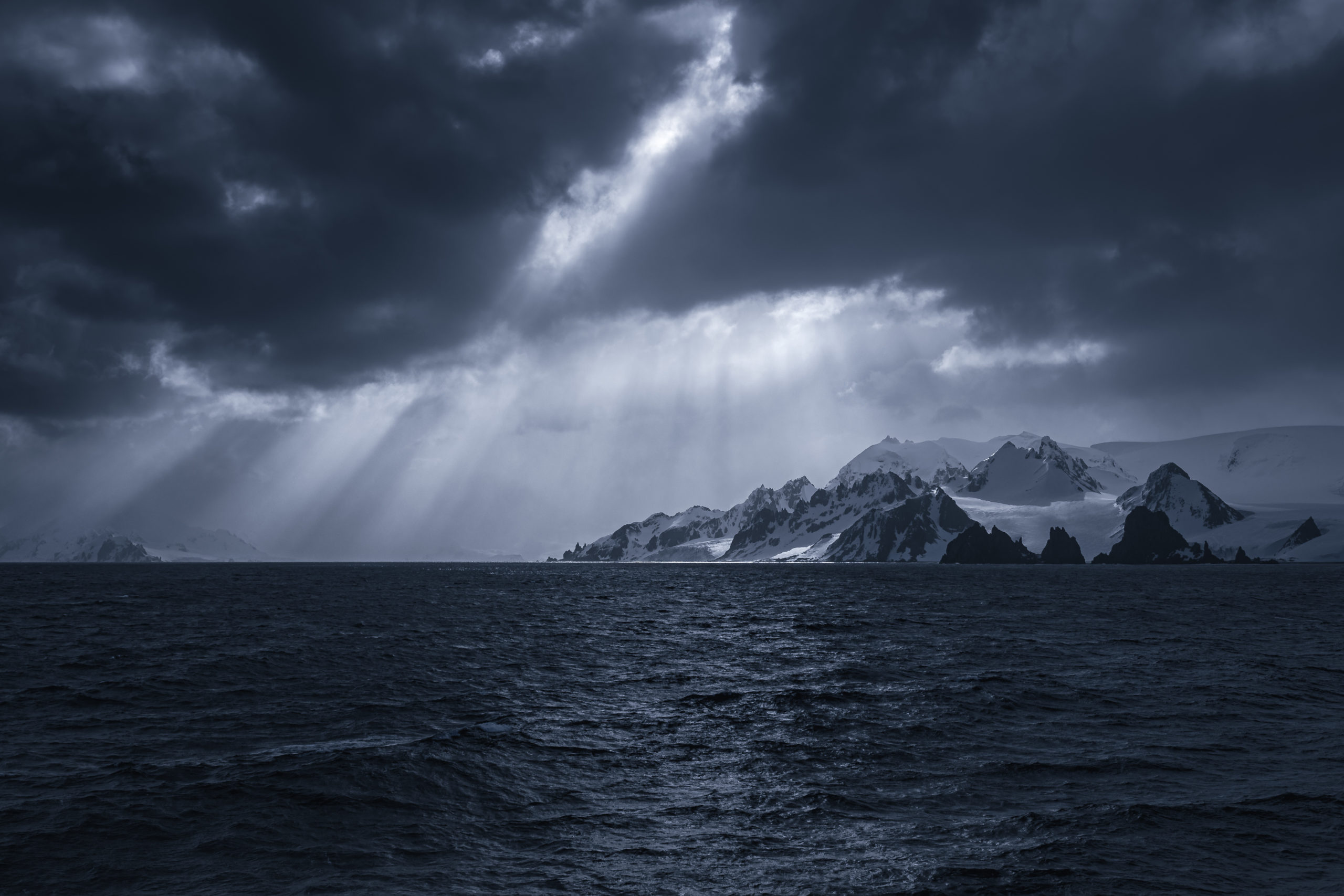 Landscape photography of light rays breaking through a stormy sky over the Shetland Islands on the Antarctic Peninsula