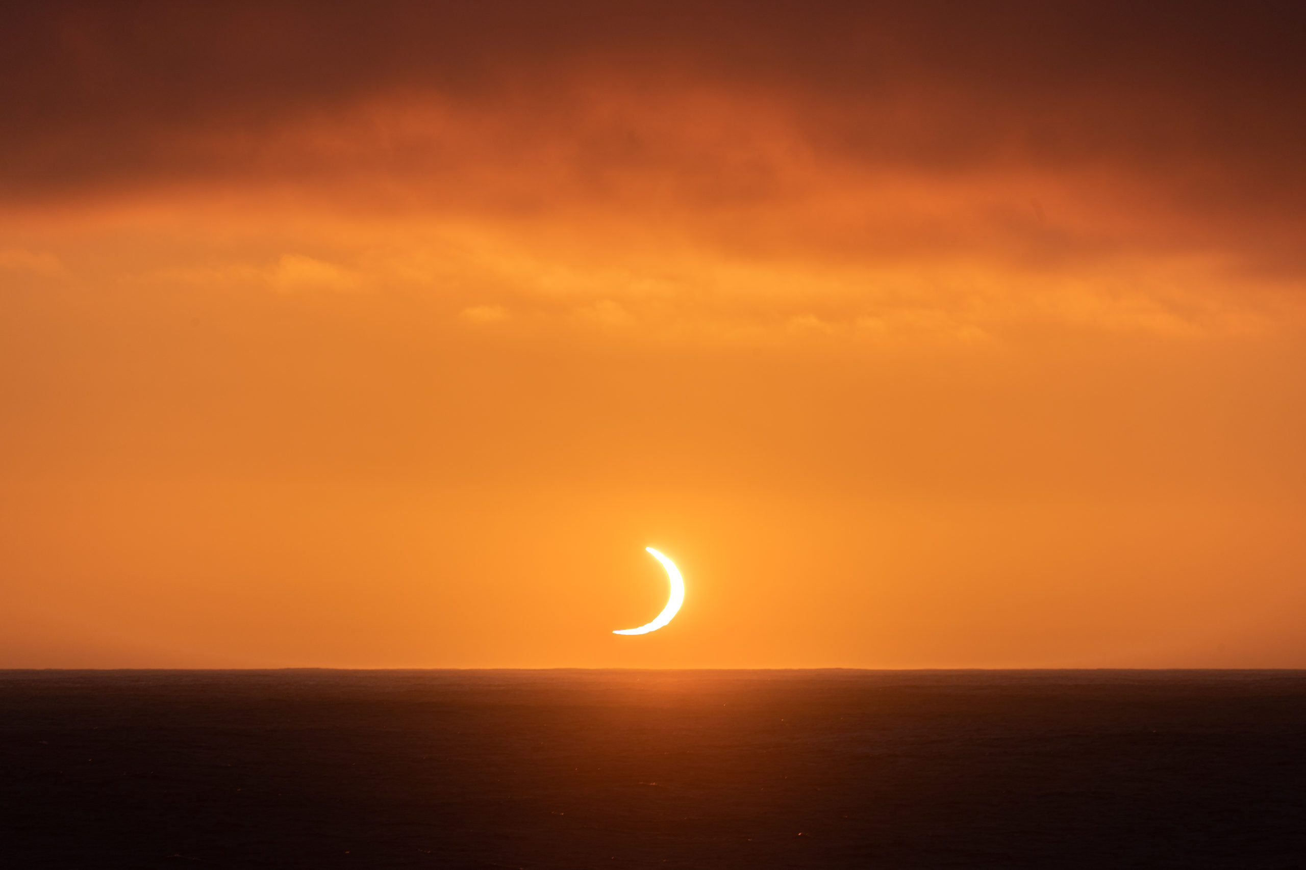 Photography of the total solar eclipse occurring just above the horizon over the ocean during sunrise in Antarctica on December 6 2021
