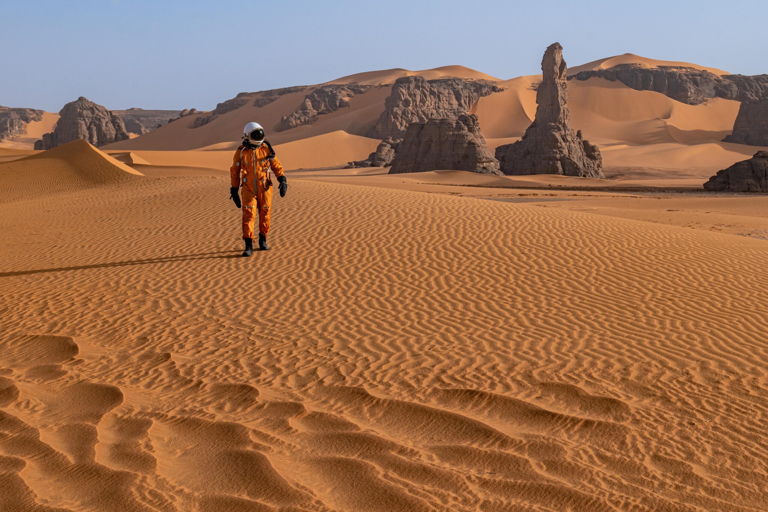 An astronaut walks through the otherworldly sand dunes of the Sahara Desert.