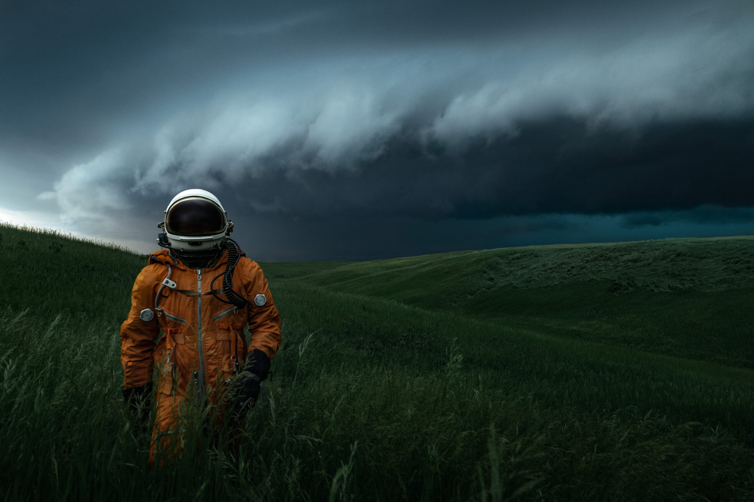 an astronaut wearing an orange space suit walks below a large storm shelf cloud