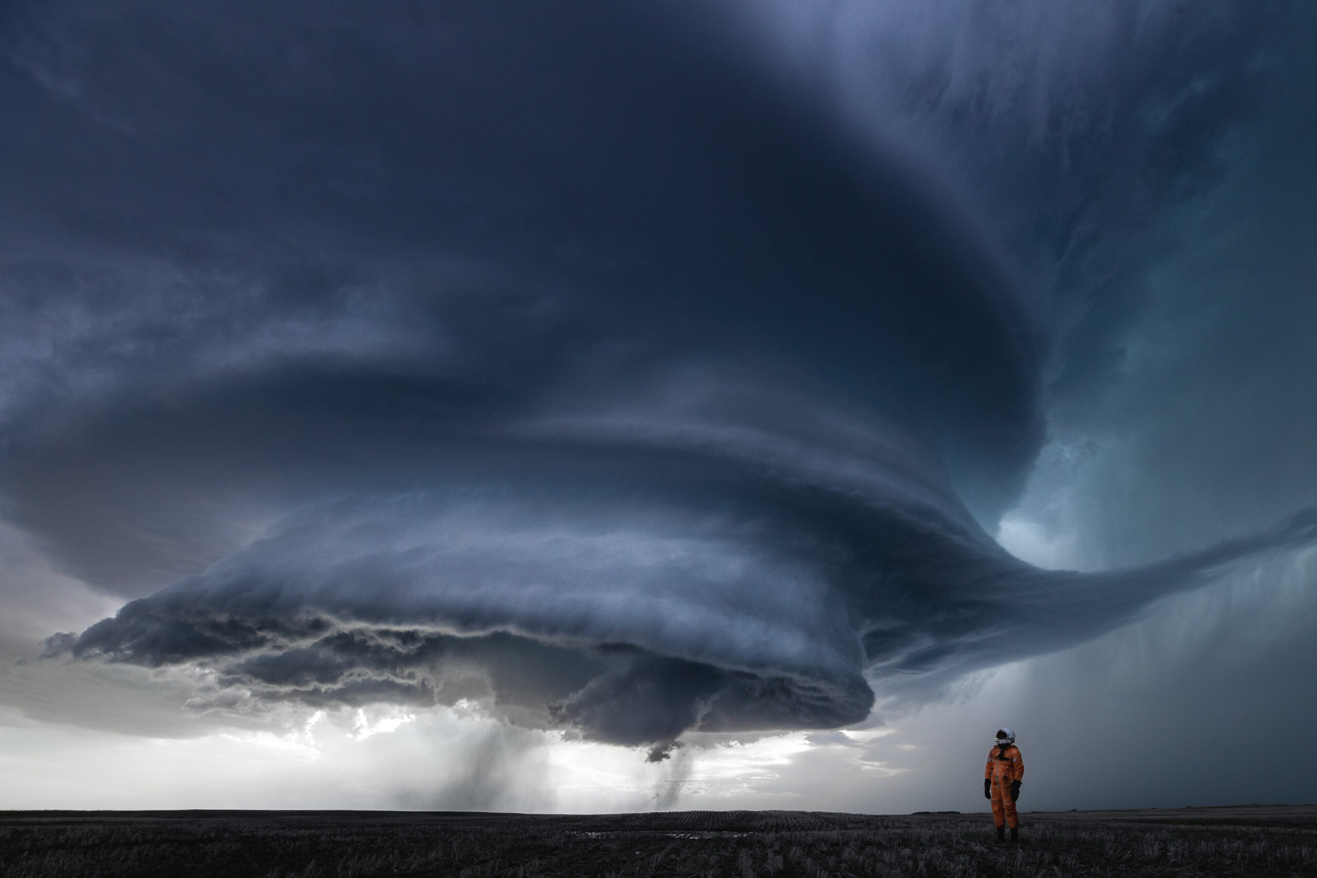 An astronaut stares up at a massive supercell resembling an alien mothership. Photographed in the plains of Saskatchewan, Canada