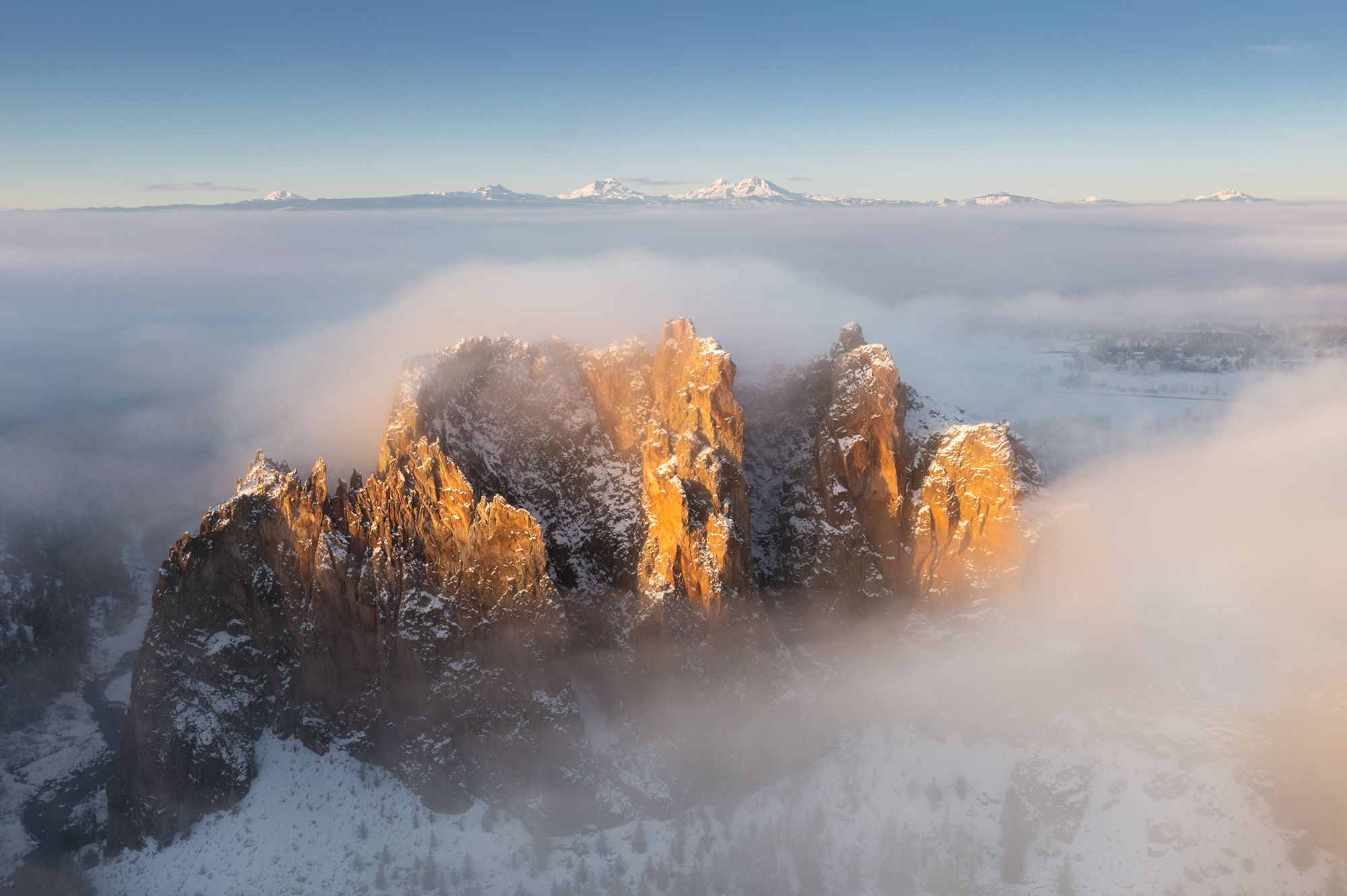 Aerial photography taken above Central Oregon's Smith Rock State Park on a foggy winter sunrise with the Cascade mountain range in the distance